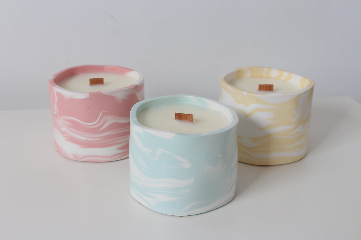 Three marbled ceramic candles in pink, blue, and yellow on a white surface.