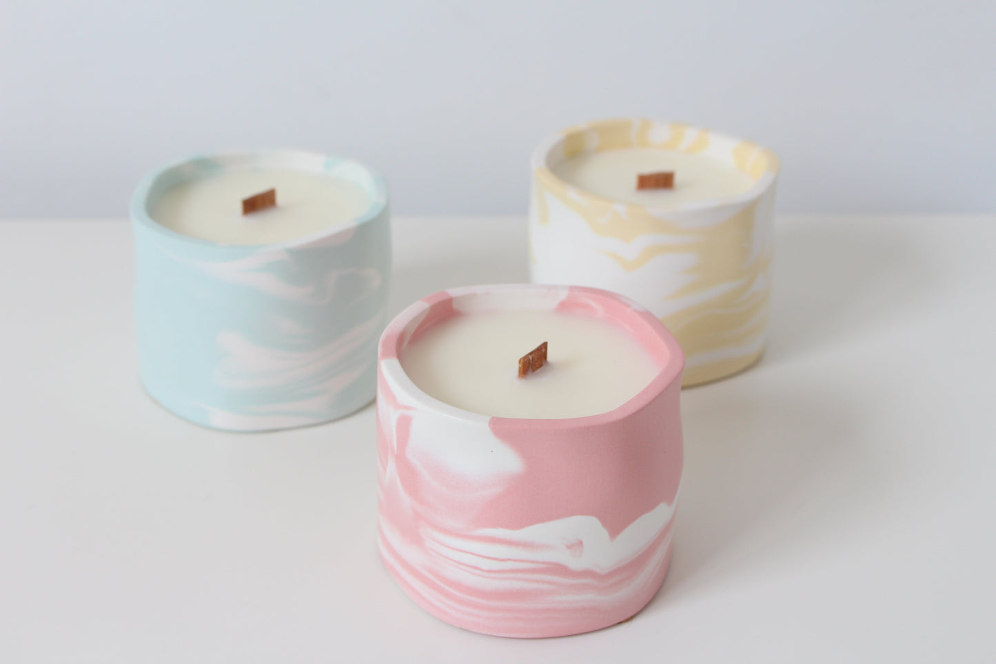 Three candles with marbled designs in pink, blue, and yellow on a white background.