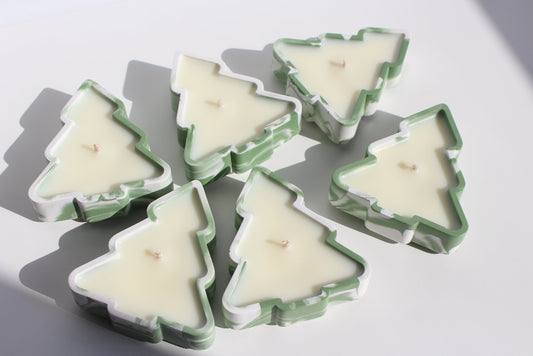 A collection of Christmas tree-shaped tea candles in green and white colors, displayed on a white surface.