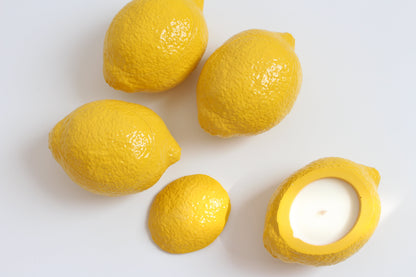 Five lemons on a white surface with one lemon cut open to reveal a candle inside.