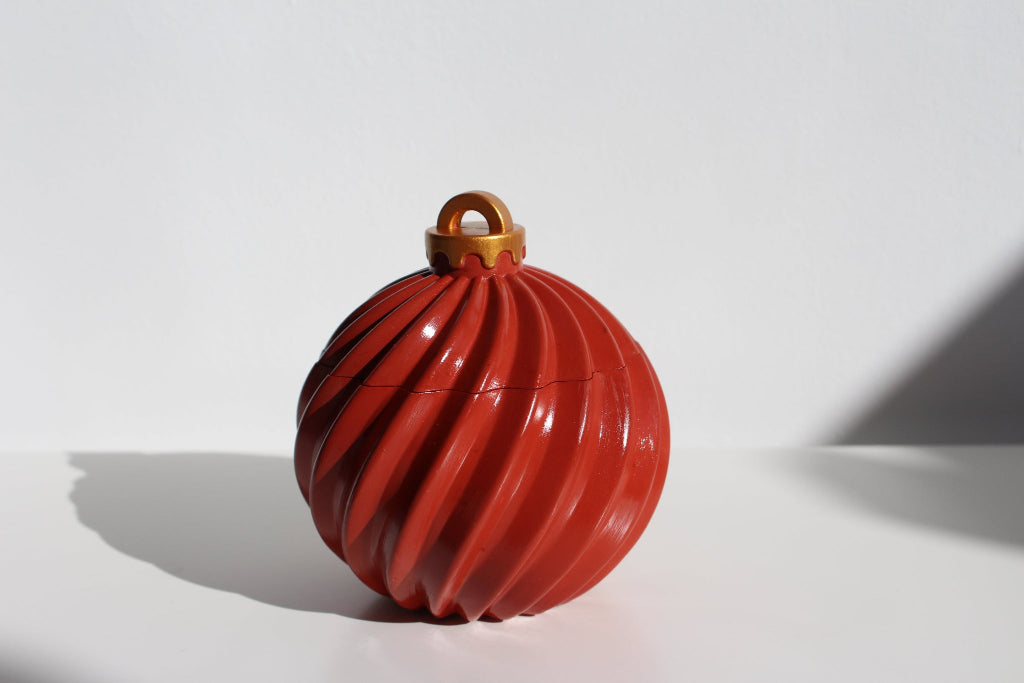 Red ribbed ornament candle with a gold hook on a white background